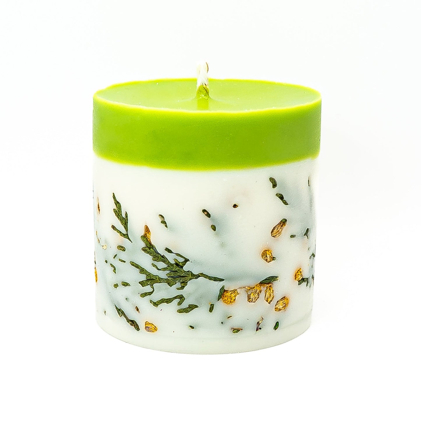 Botanical soy pillar candle with dried greenery embedded in wax and bright green upper layer.