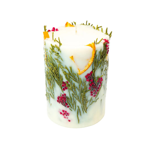 Festive soy wax pillar candle with dried orange slices, delicate thuja branches and red berry clusters embedded in creamy wax.