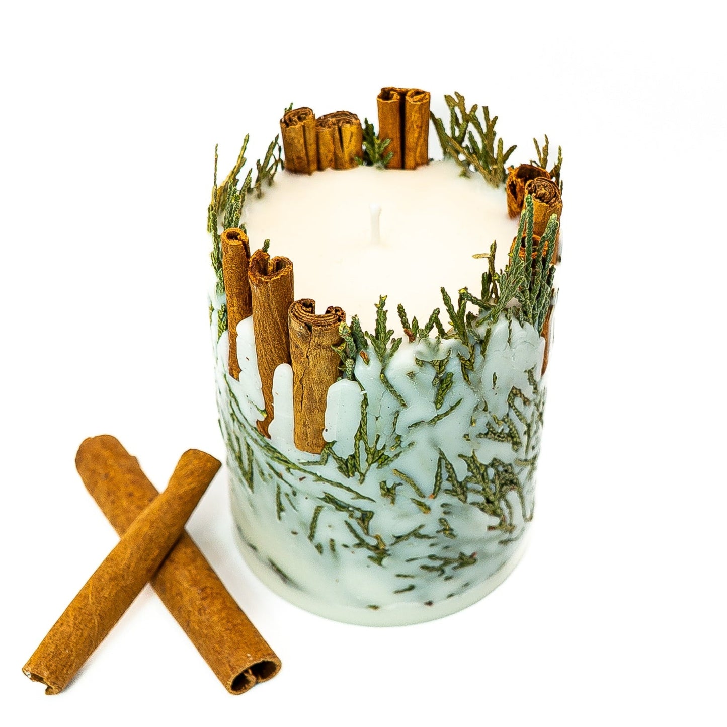 Seasonal winter botanical pillar candle with cinnamon sticks and evergreen elements in soy wax.