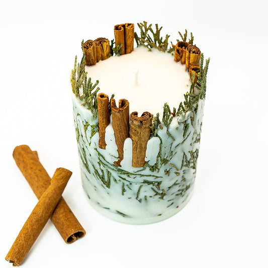 Winter botanical pillar candle with whole cinnamon sticks and evergreen leaves in soy wax.