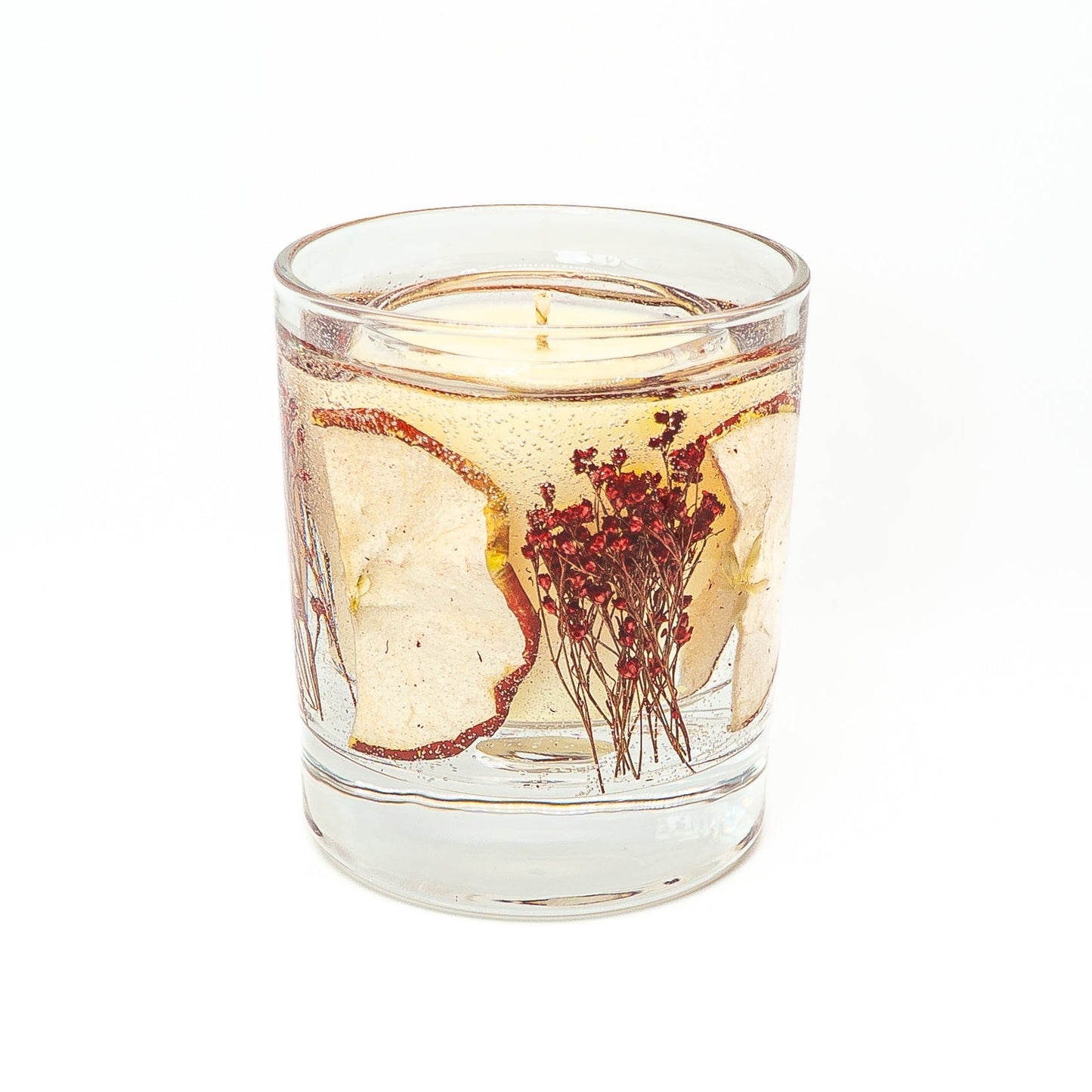Soy wax candle with transparent gel wax layer containing dried red apple slice in a glass jar with bamboo lid.