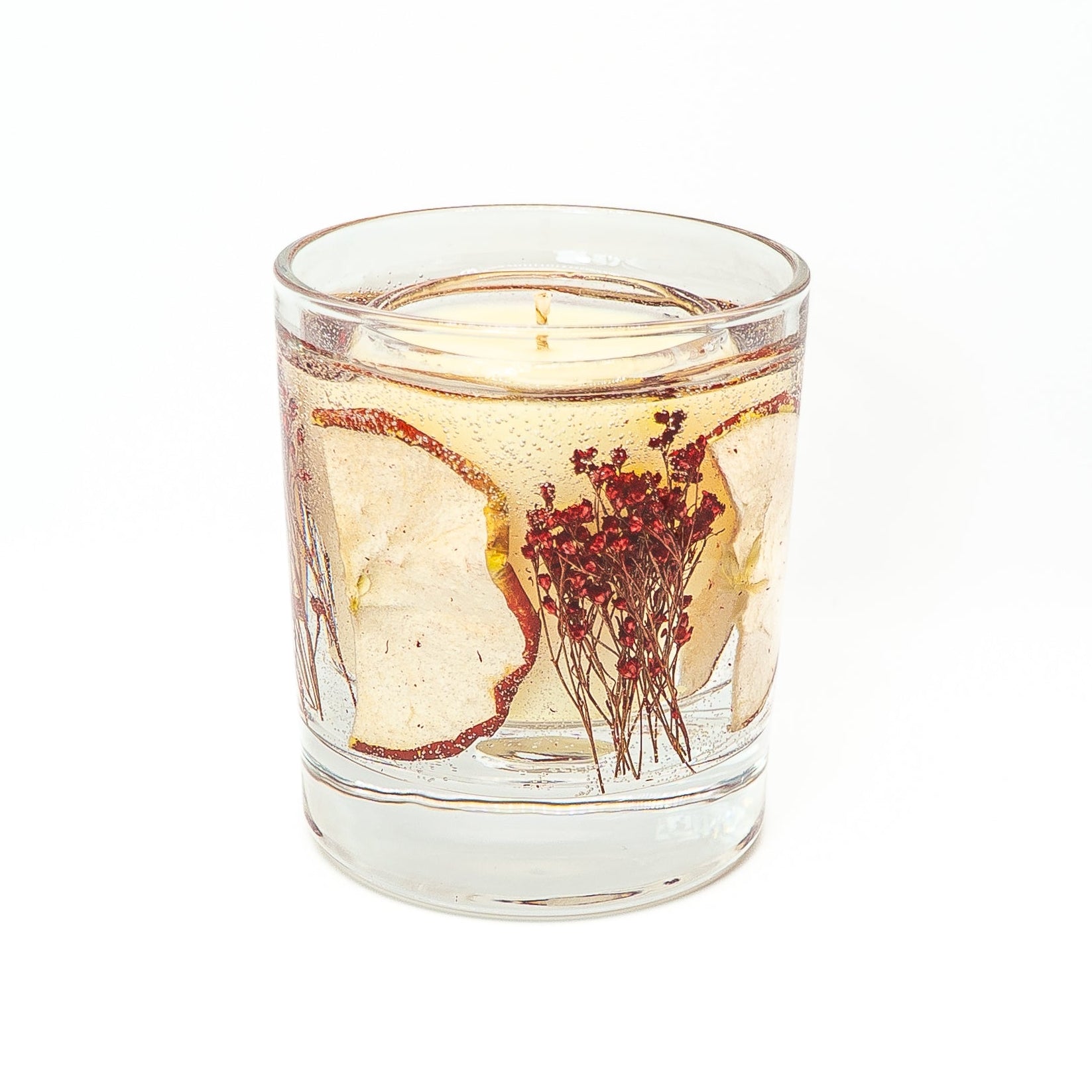 Soy wax candle with transparent gel wax layer containing dried red apple slice in a glass jar with bamboo lid.
