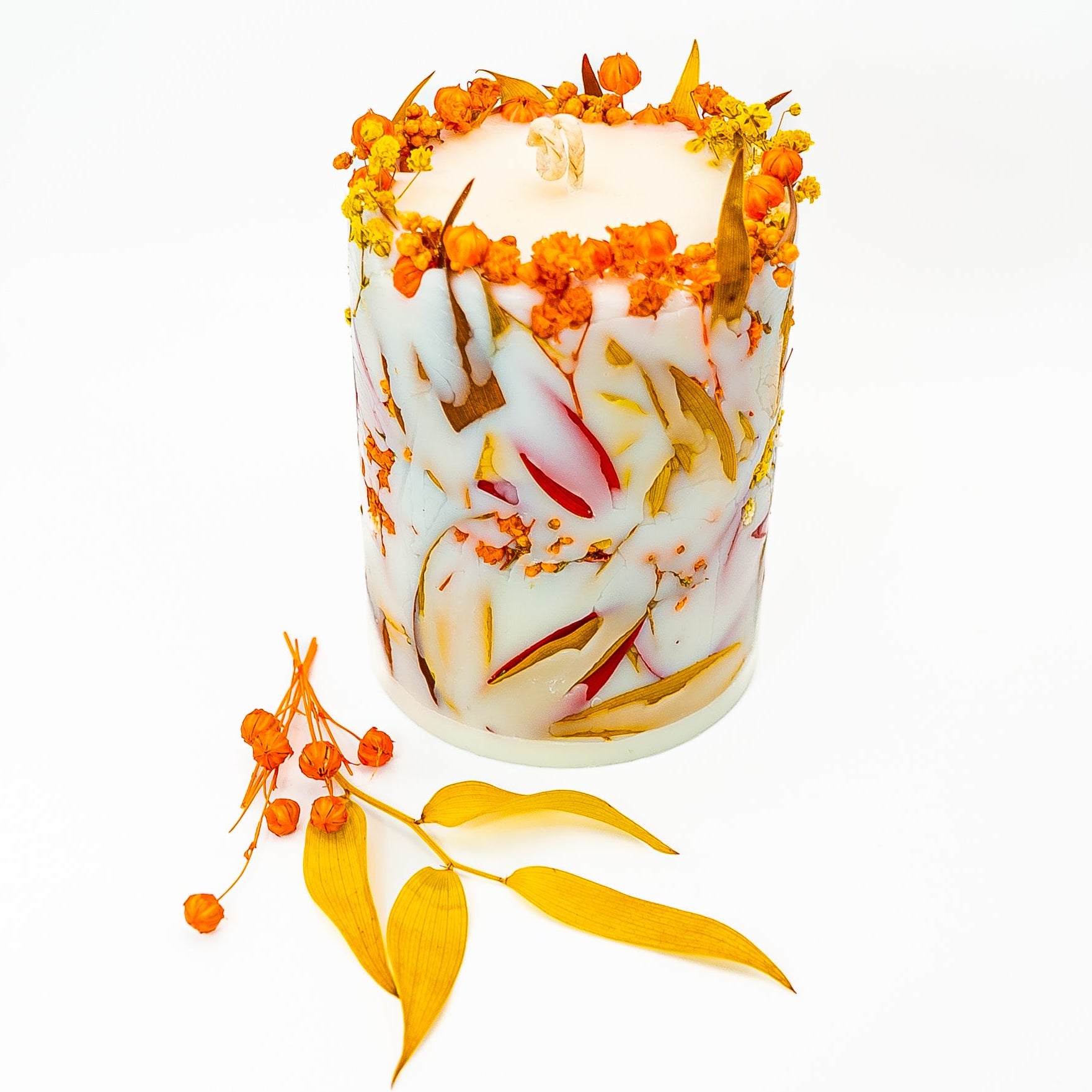 Hand-poured autumn botanical pillar candle with dried flowers and leaves embedded in soy wax.