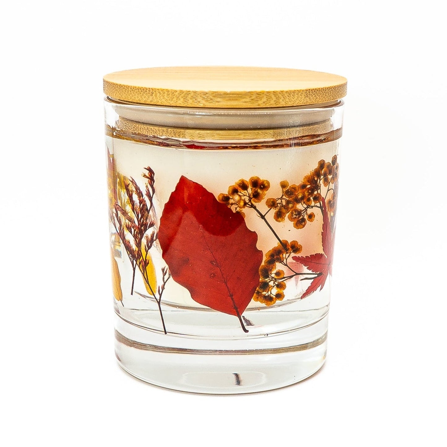 Soy wax candle with clear gel wax layer decorated with red autumn leaves and dried botanicals in a glass jar with bamboo lid.