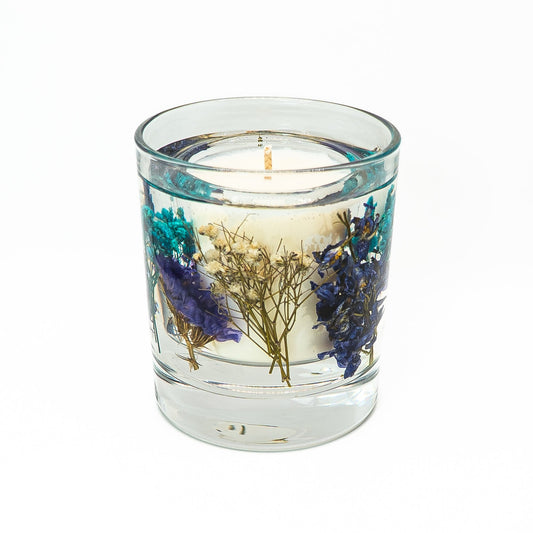 Decorative soy wax candle with transparent gel wax containing preserved blue flowers and dried botanical stems.