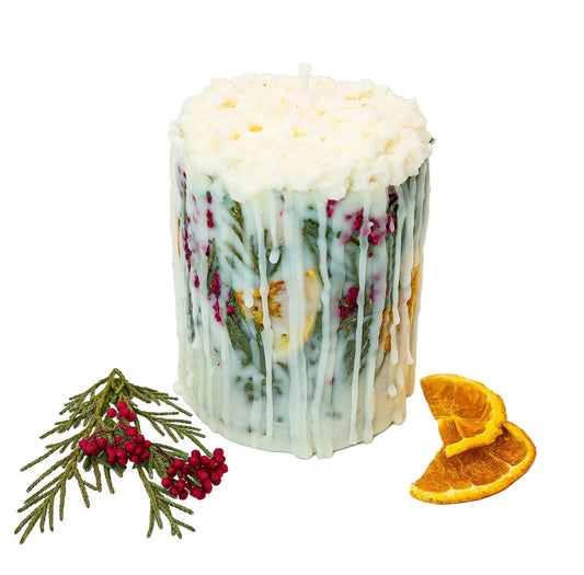 Botanical Christmas candle with a textured cream wax top, green foliage and red berries, beside dried orange slices and an evergreen sprig.