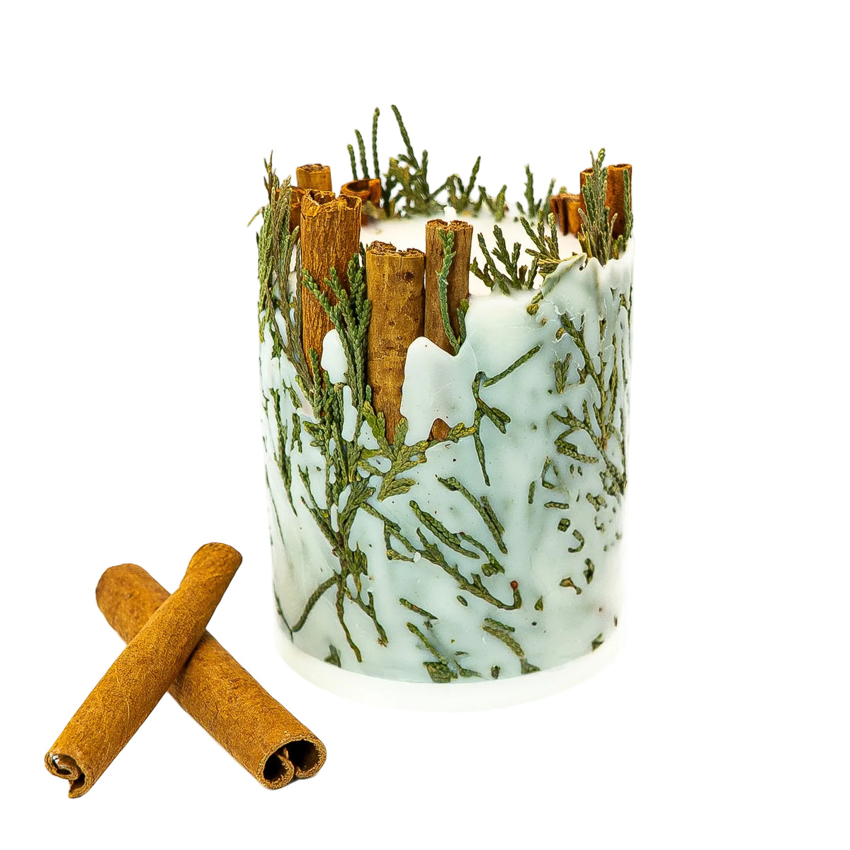 Side view of a soy wax Christmas pillar candle with delicate evergreen foliage and cinnamon sticks, photographed on white. 