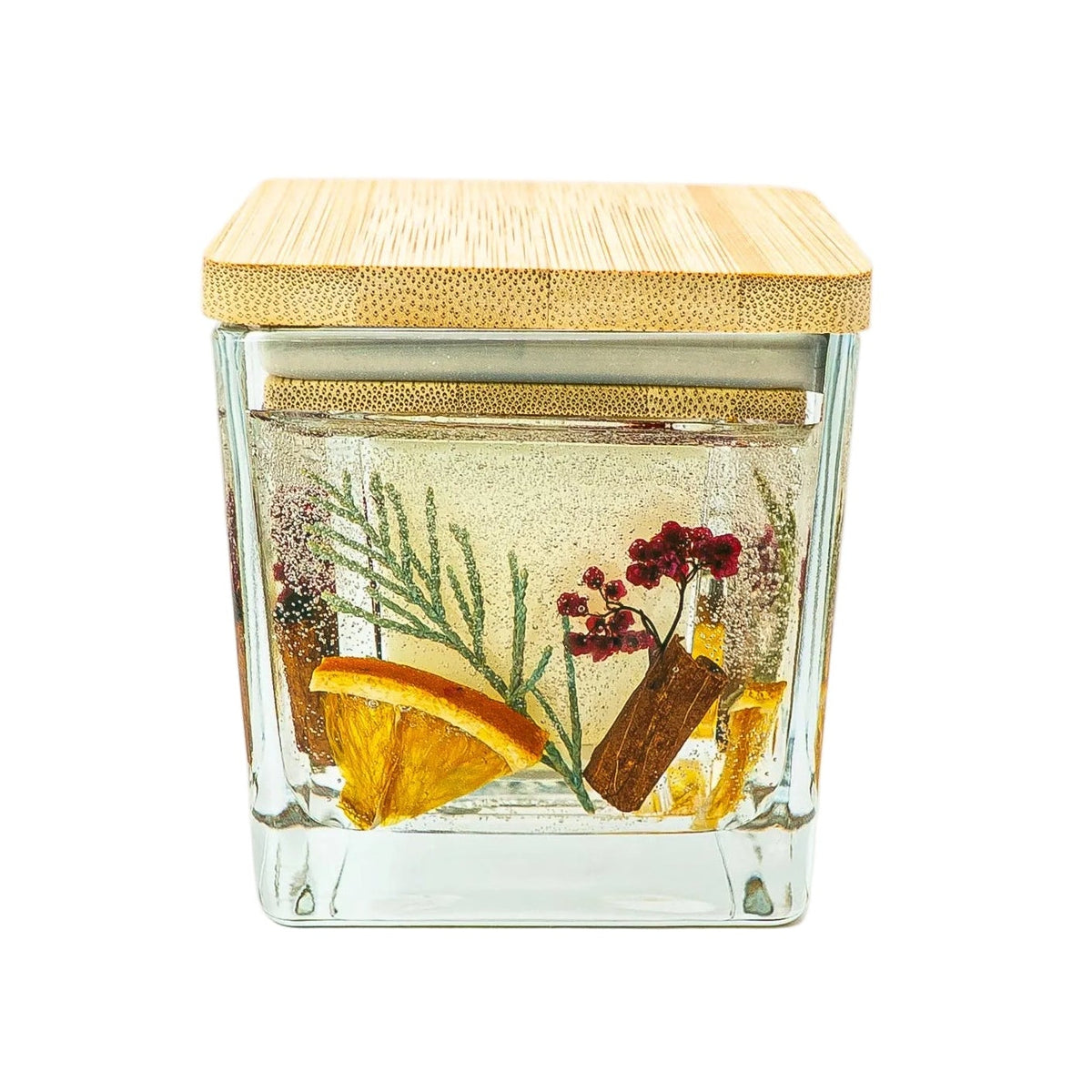 Handmade Christmas botanical candle in a square glass jar with a wooden lid, dried orange, cinnamon, thuja and red berries.