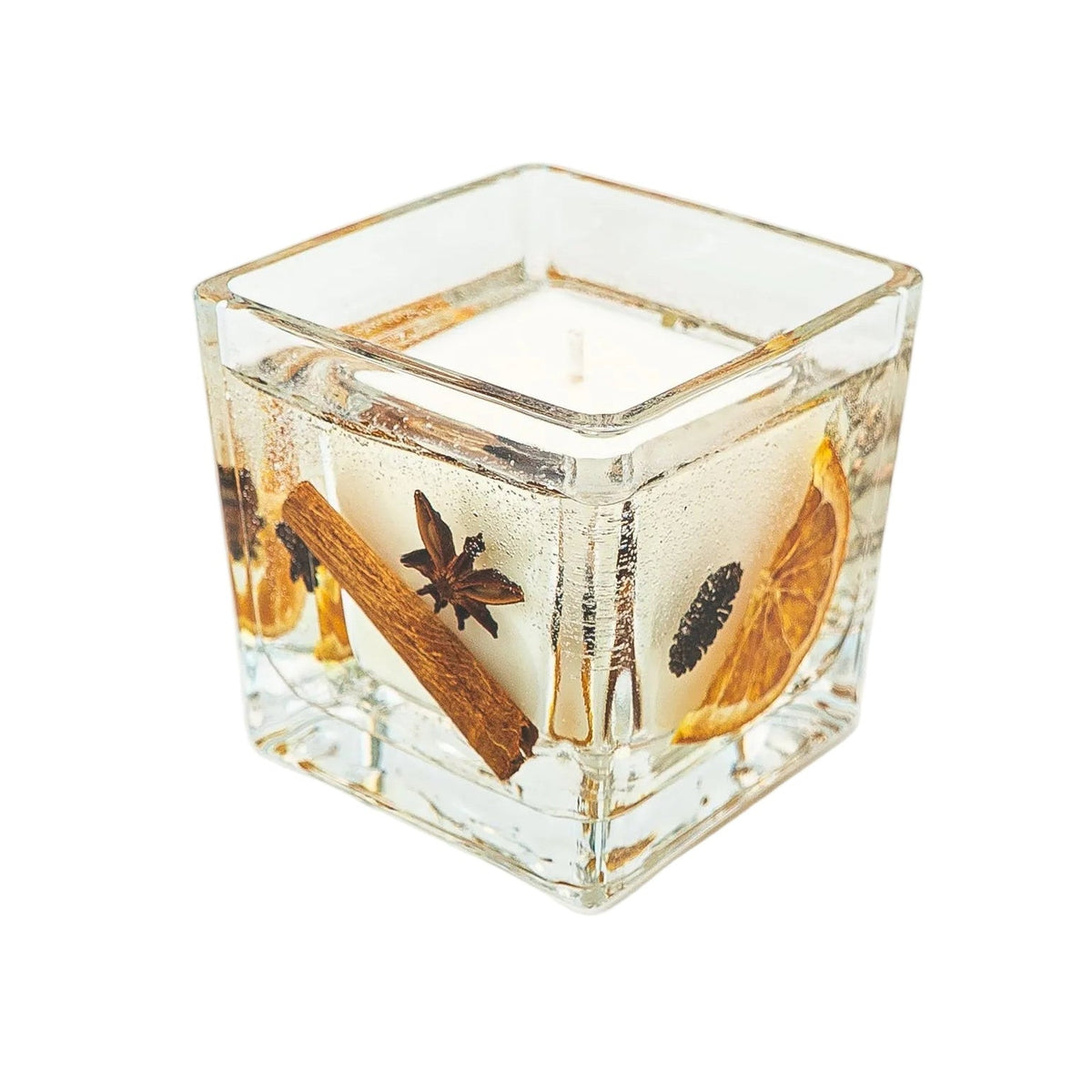 Angled view of a Christmas jar candle with cinnamon, star anise, a pine cone and dried orange around a soy wax centre.