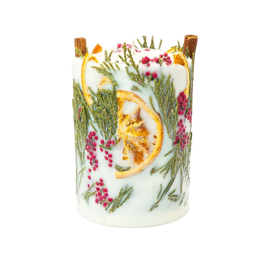 Cream soy wax Christmas pillar candle with a large dried orange slice, thuja foliage, red berries and cinnamon sticks on a white background.