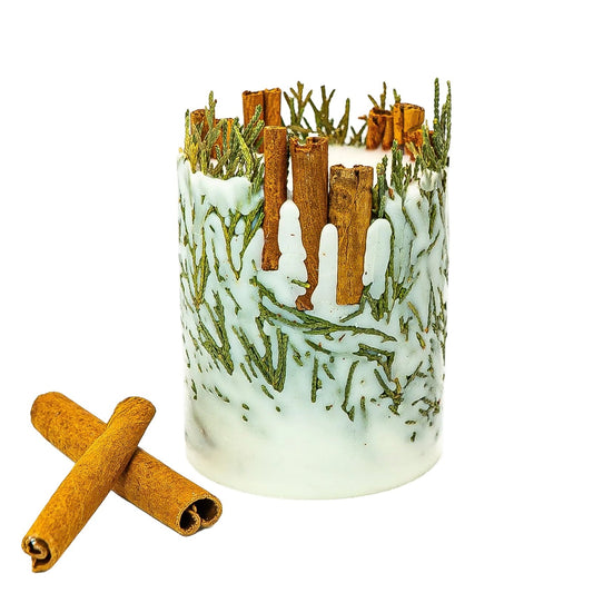 Cream soy wax Christmas candle with cinnamon sticks and embedded evergreen sprigs, beside two crossed cinnamon sticks on a white background.