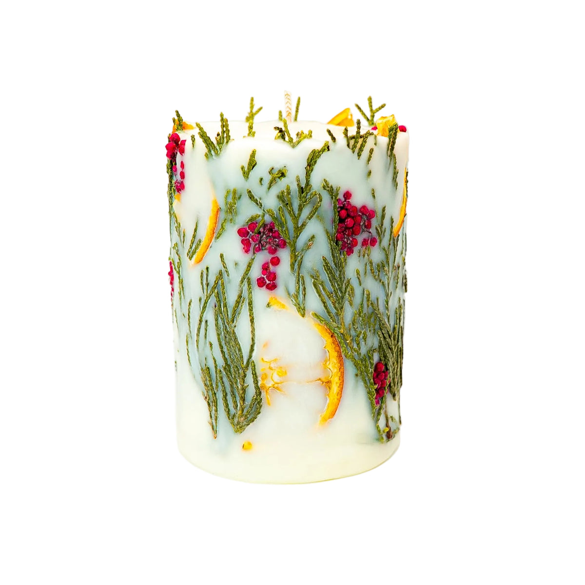 Christmas pillar candle showing a large dried orange slice near the top, surrounded by green thuja and clusters of red berries.
