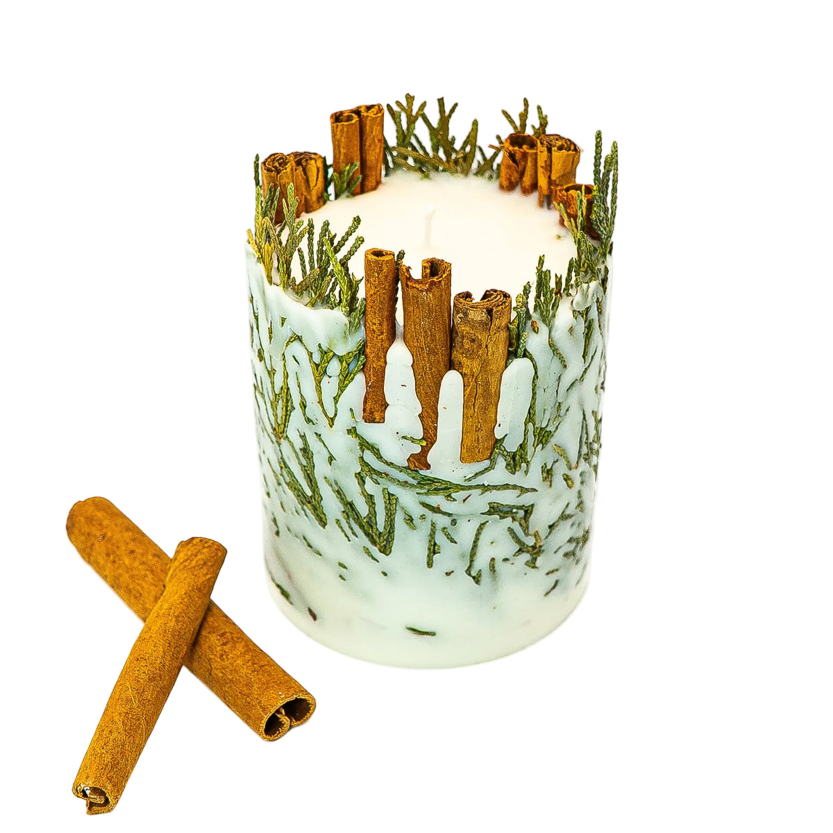 Cinnamon and evergreen botanical Christmas candle with its cotton wick visible, beside crossed cinnamon sticks on a white background.