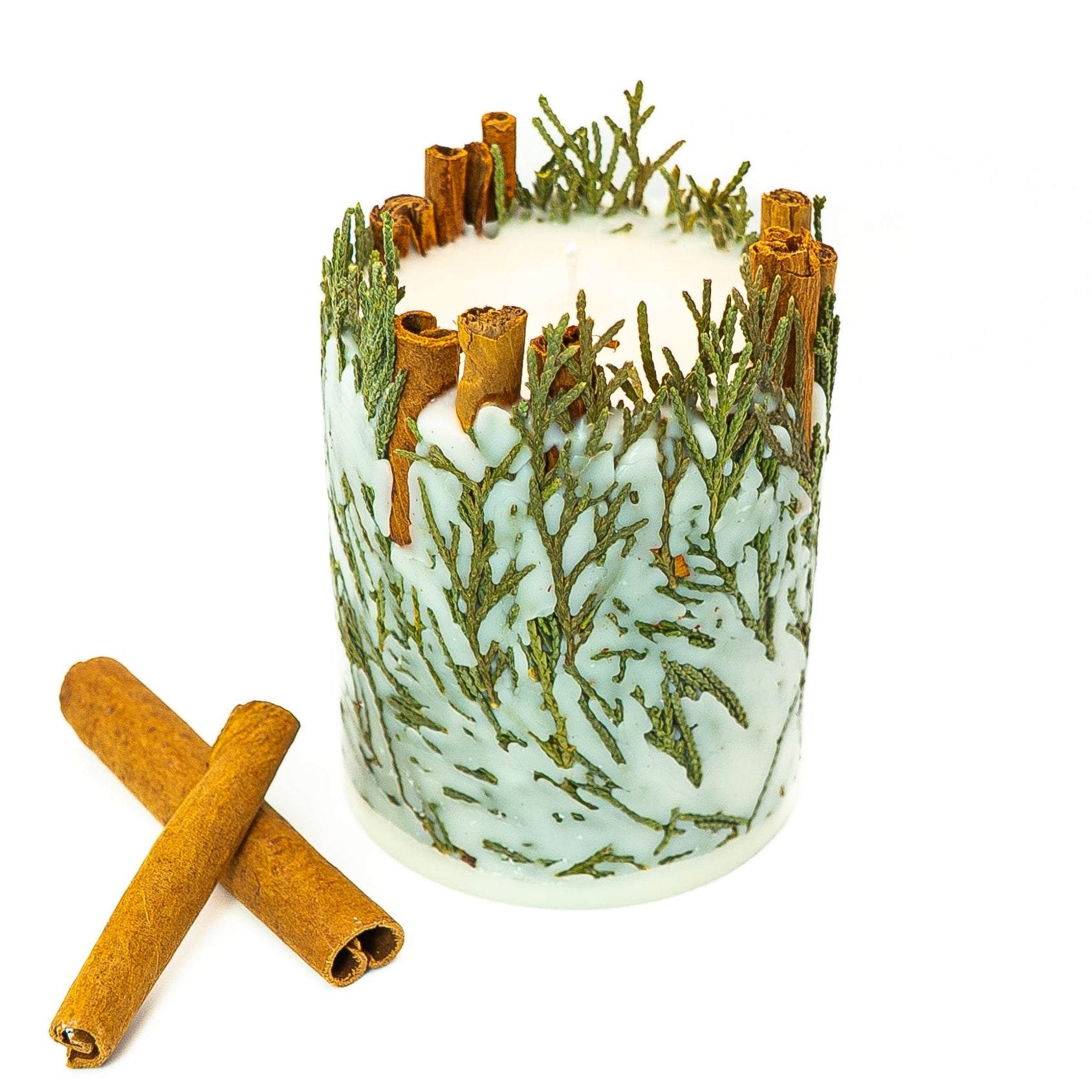 Soy wax pillar candle featuring natural cinnamon sticks and evergreen sprigs for winter décor.