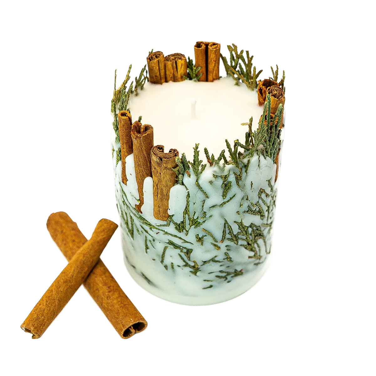 Angled view of a cinnamon and evergreen soy wax Christmas candle with two loose cinnamon sticks beside it.