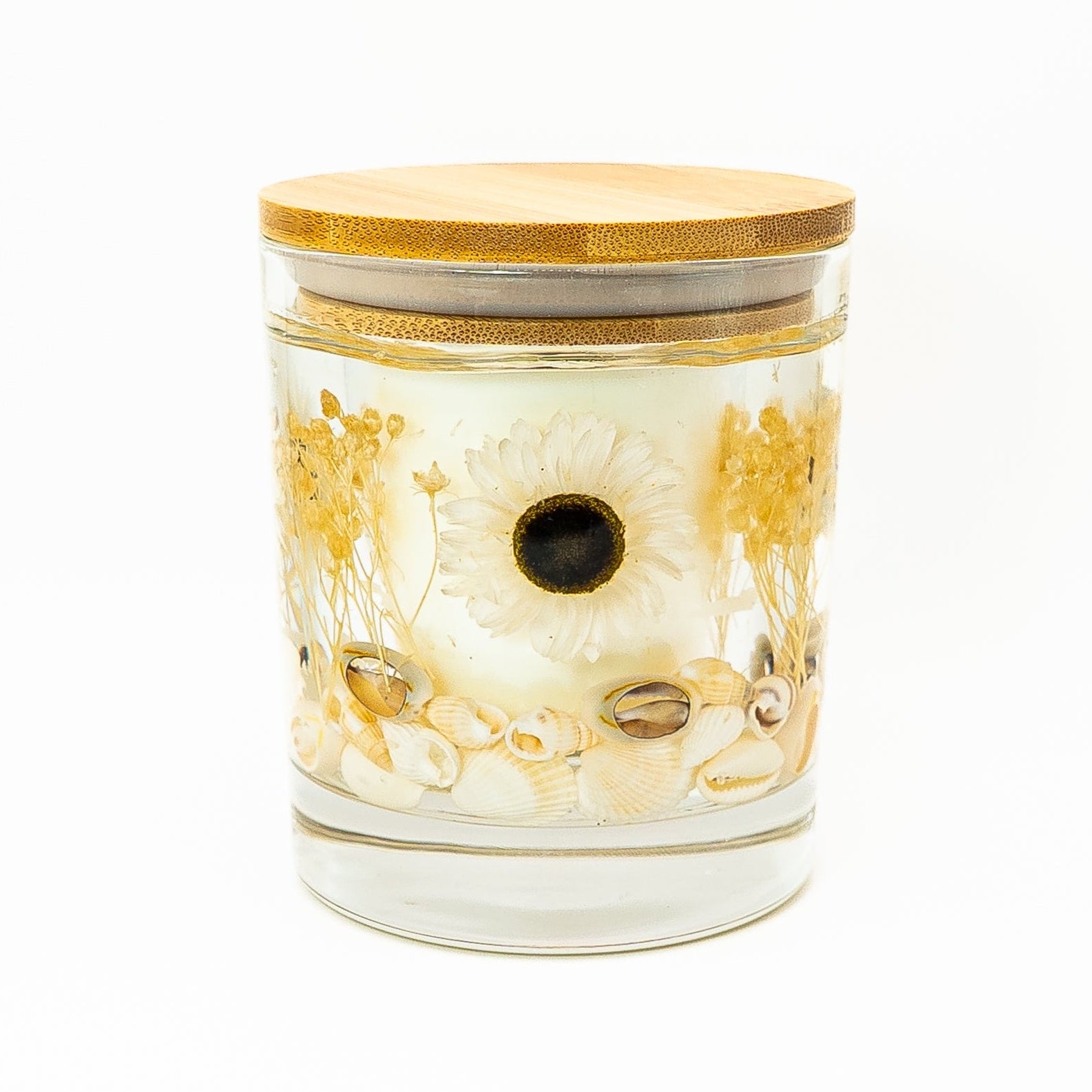 Handmade gel candle in a glass jar with bamboo lid, decorated with a white daisy flower and seashells.