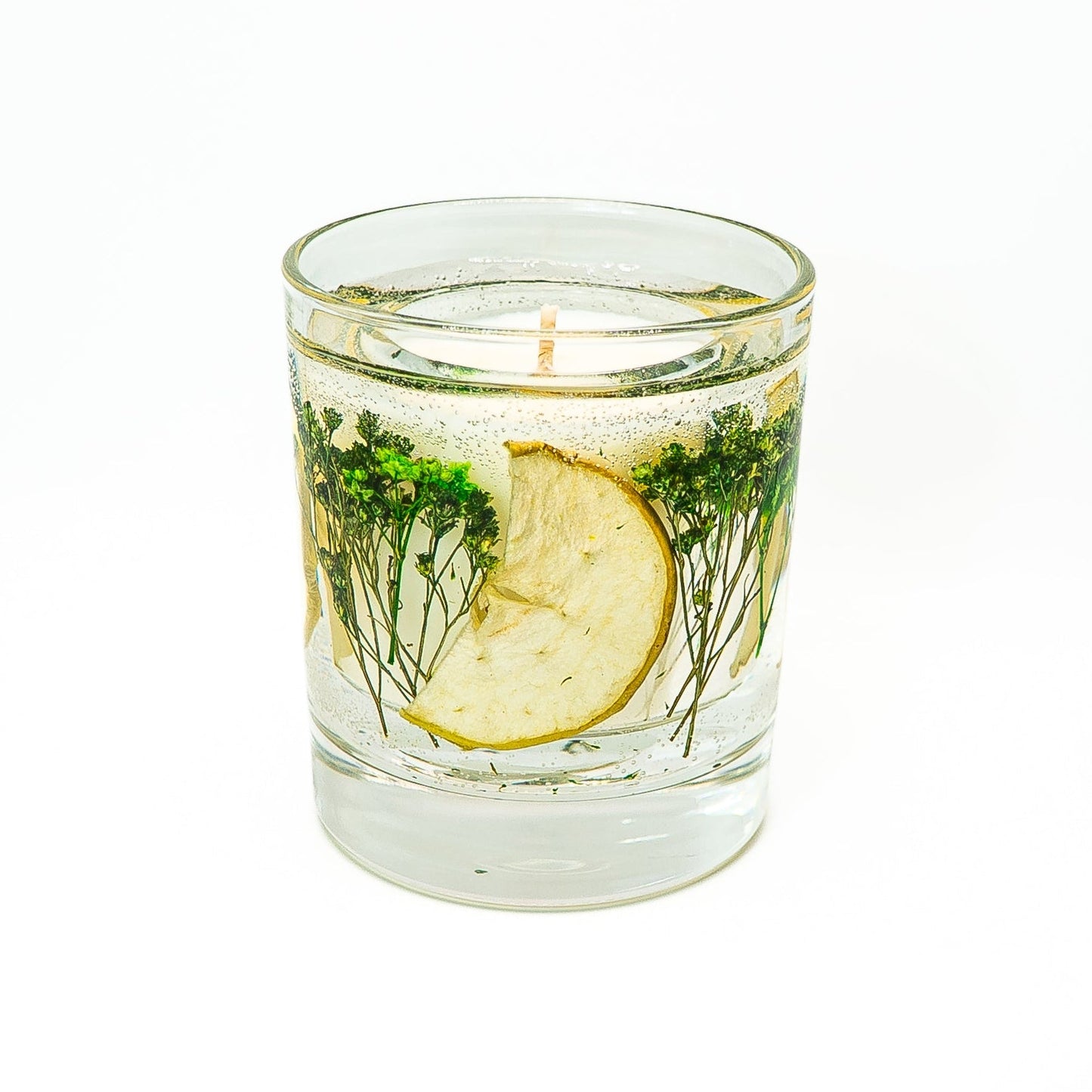 Decorative soy wax candle with transparent gel wax containing dried green apple slices and preserved green botanicals.