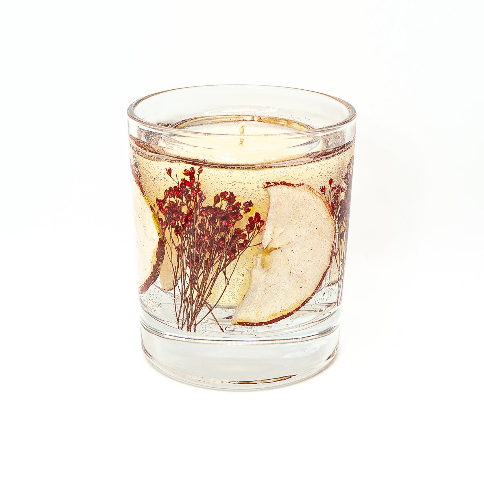 Decorative soy wax candle with transparent gel wax containing dried red apple slice and preserved red botanicals.
