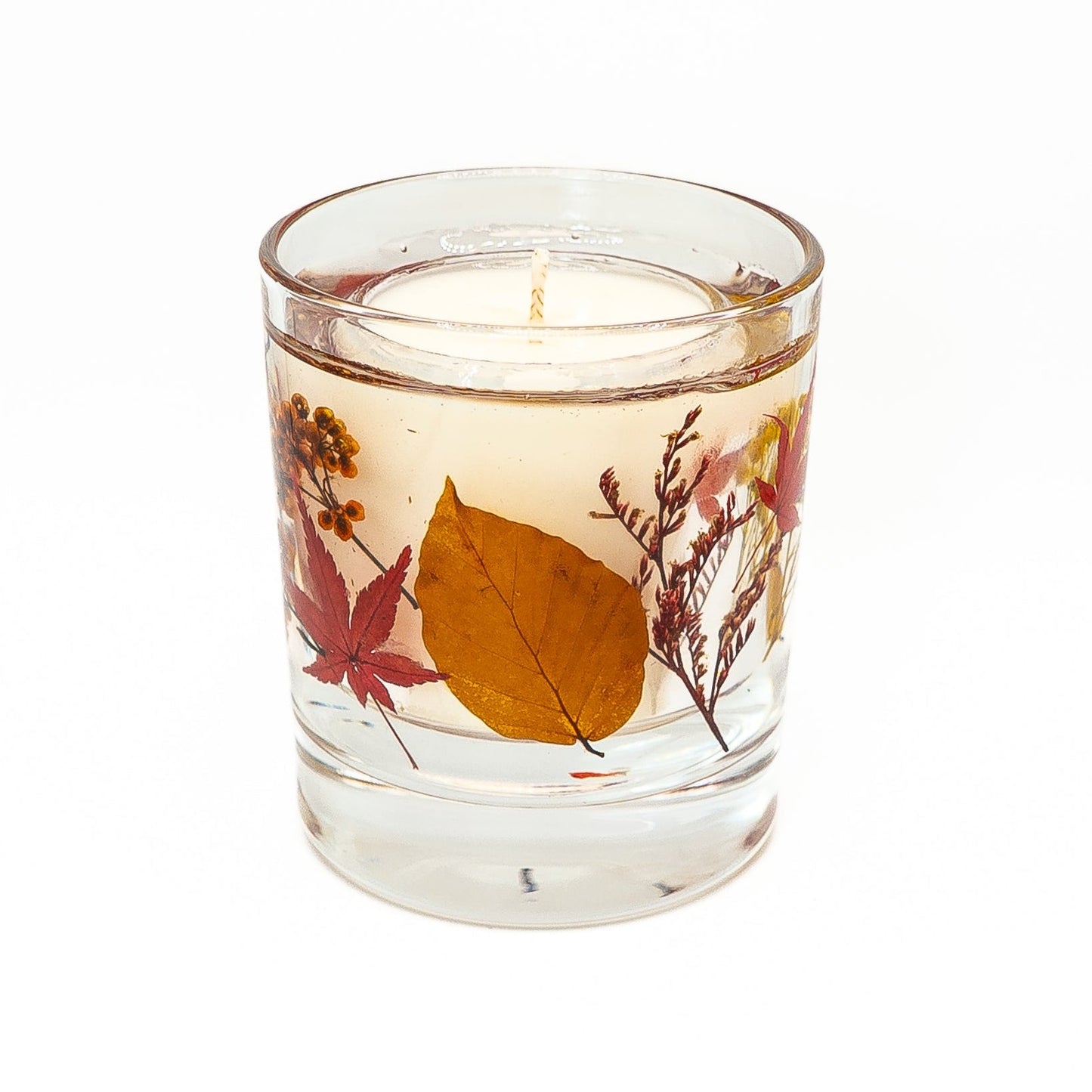 Decorative soy wax candle with transparent gel wax featuring pressed autumn leaves and dried botanical accents.