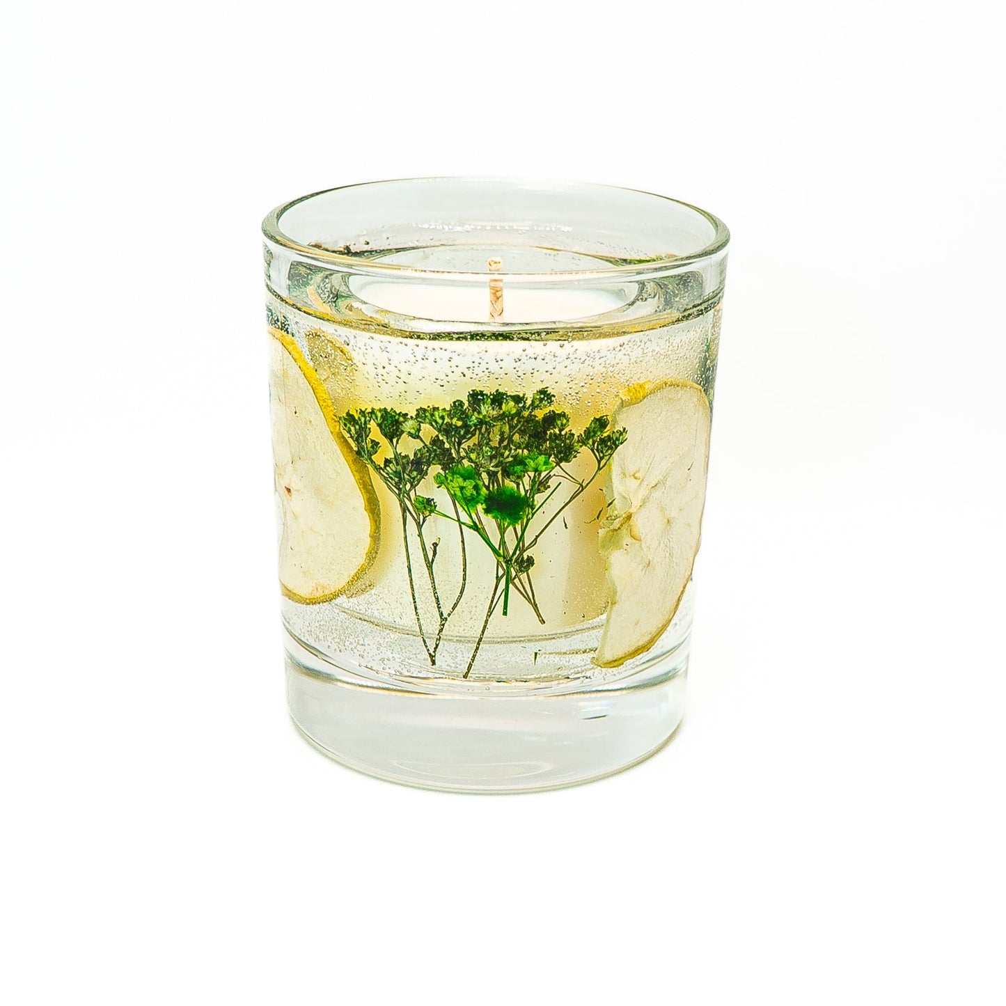 Soy wax candle with transparent gel wax decorated with dried green apple slices in a glass jar with bamboo lid.