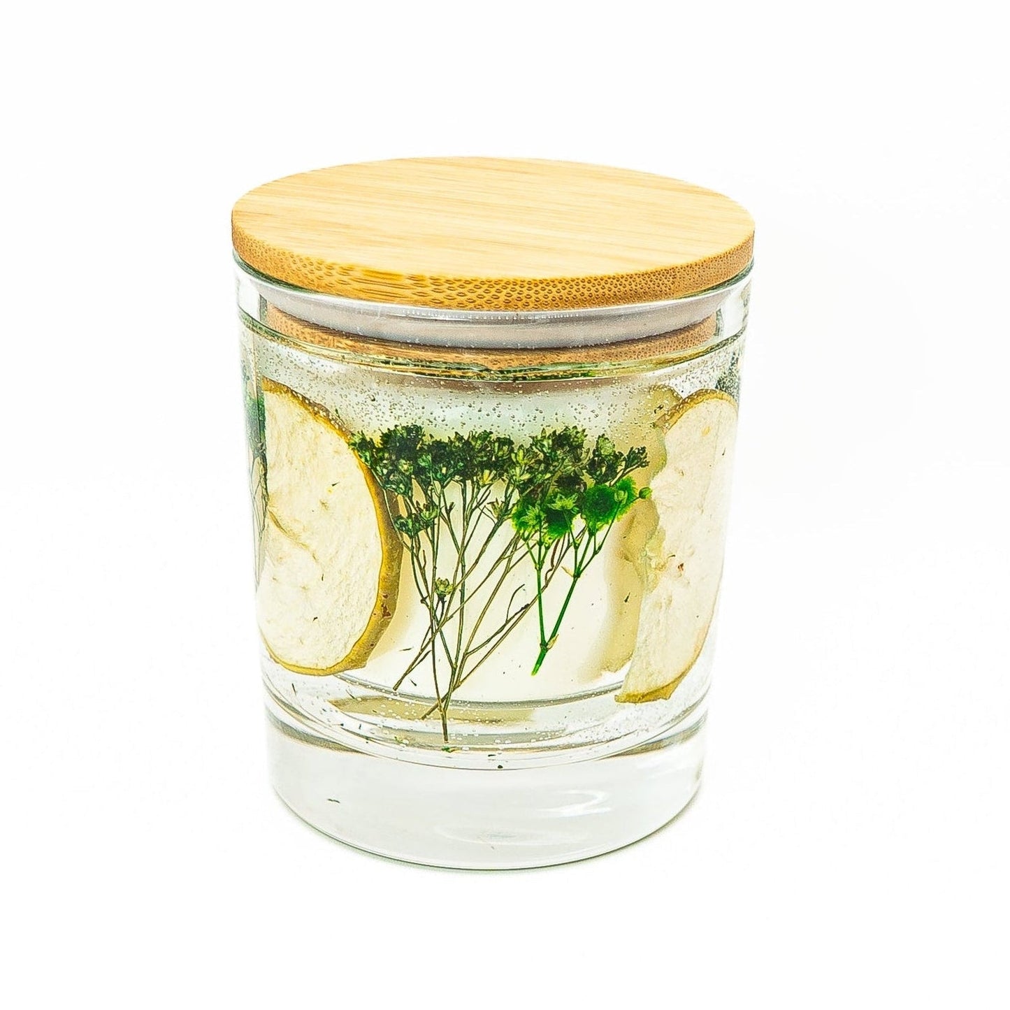 Soy wax candle with clear gel wax layer featuring dried green apple slices and botanical decorations in a glass jar with bamboo lid.