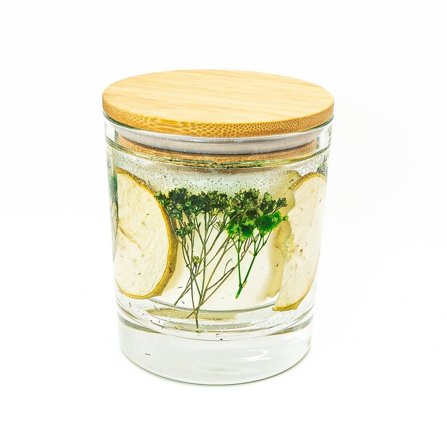 Soy wax candle with clear gel wax layer featuring dried green apple slices and botanical decorations in a glass jar with bamboo lid.