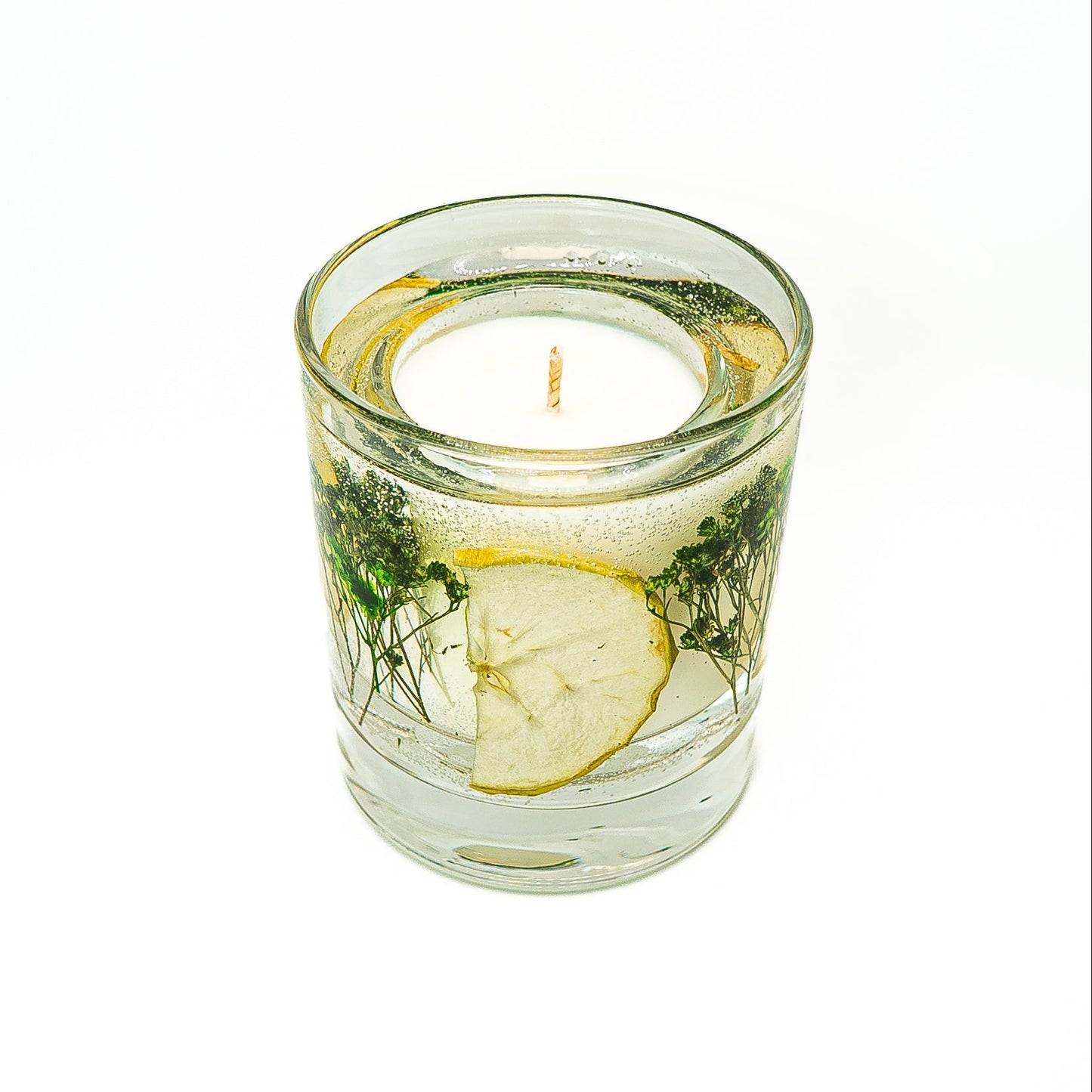 Soy wax candle with gel wax outer layer decorated with dried green apple slices and natural botanical elements.