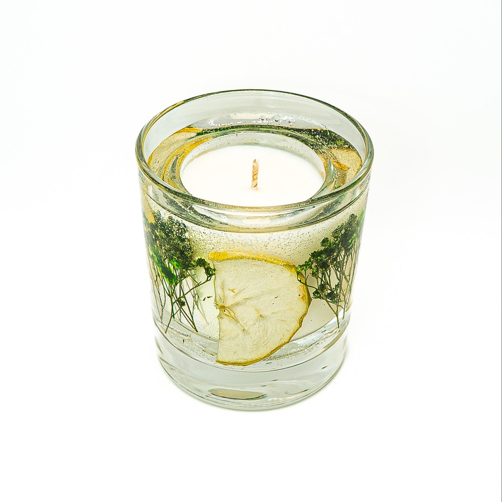 Soy wax candle with gel wax outer layer decorated with dried green apple slices and natural botanical elements.