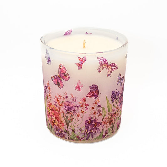Hand-poured soy wax candle in frosted glass container featuring colourful butterfly and floral pattern design.
