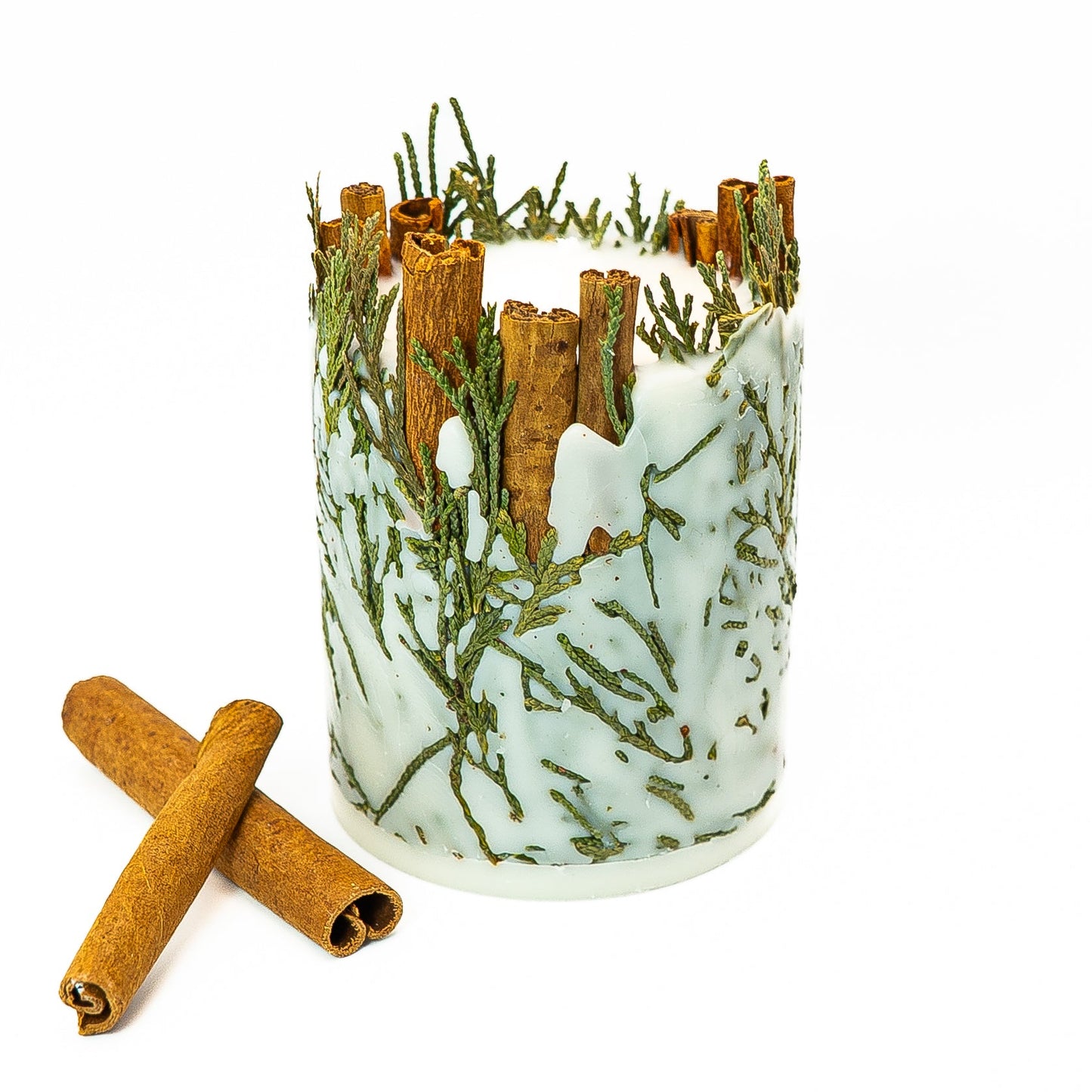 Hand-poured soy wax pillar candle decorated with cinnamon sticks and evergreen botanical elements.