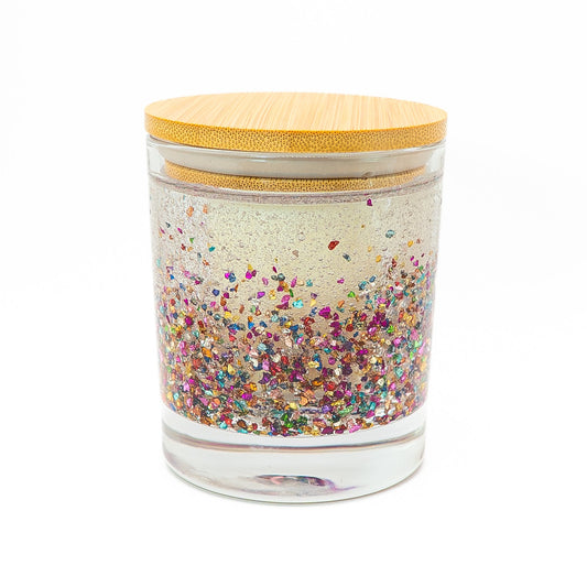 Hand-poured soy wax candle in a clear glass jar with colourful glitter and wooden lid.