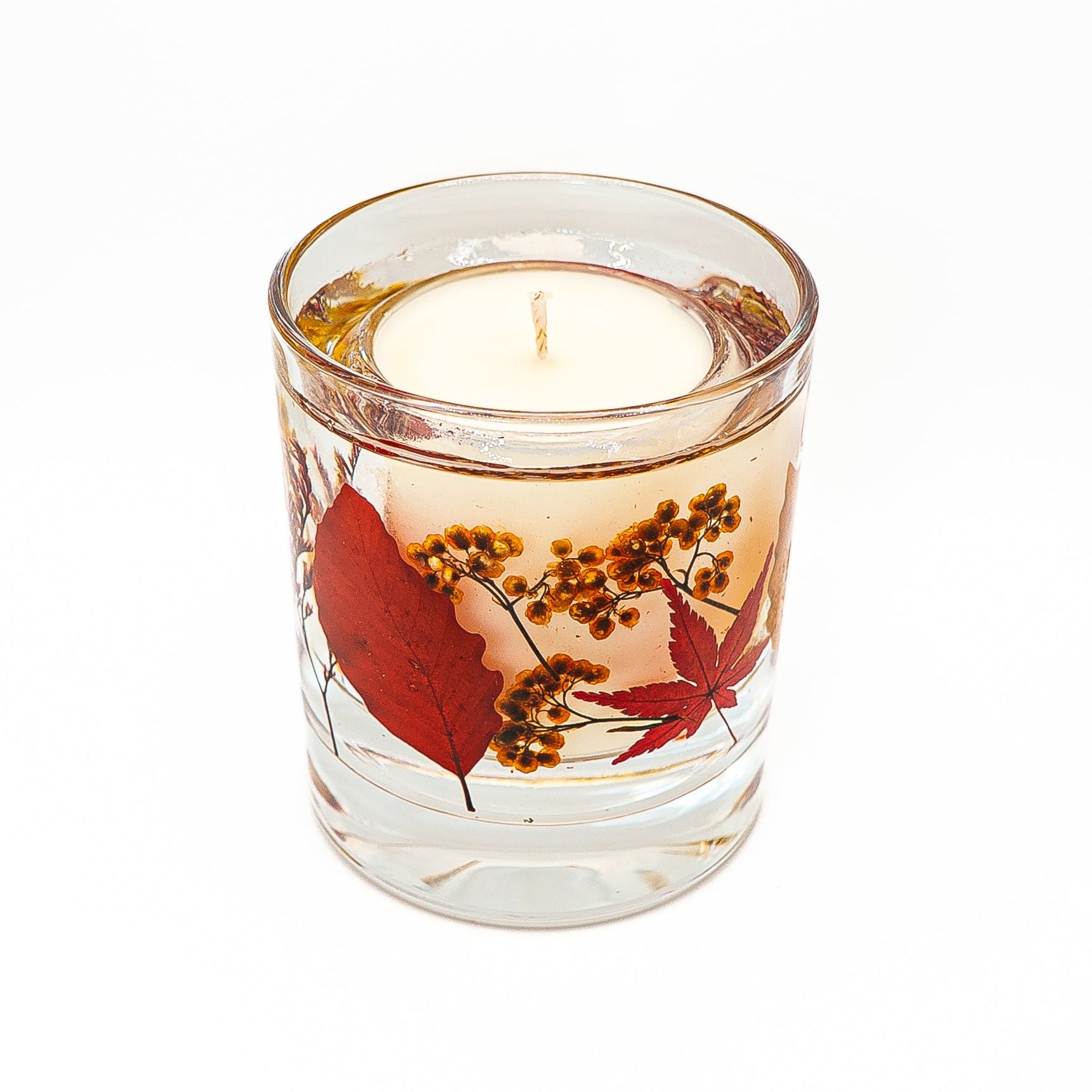 Handmade soy wax candle with decorative gel wax layer containing red autumn leaves and dried botanicals.