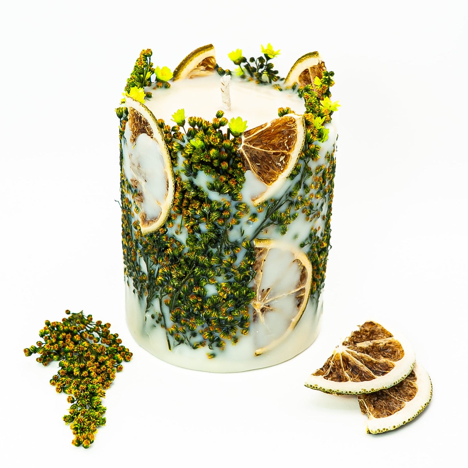 Handmade botanical pillar candle with dried citrus pieces and green foliage embedded in soy wax.