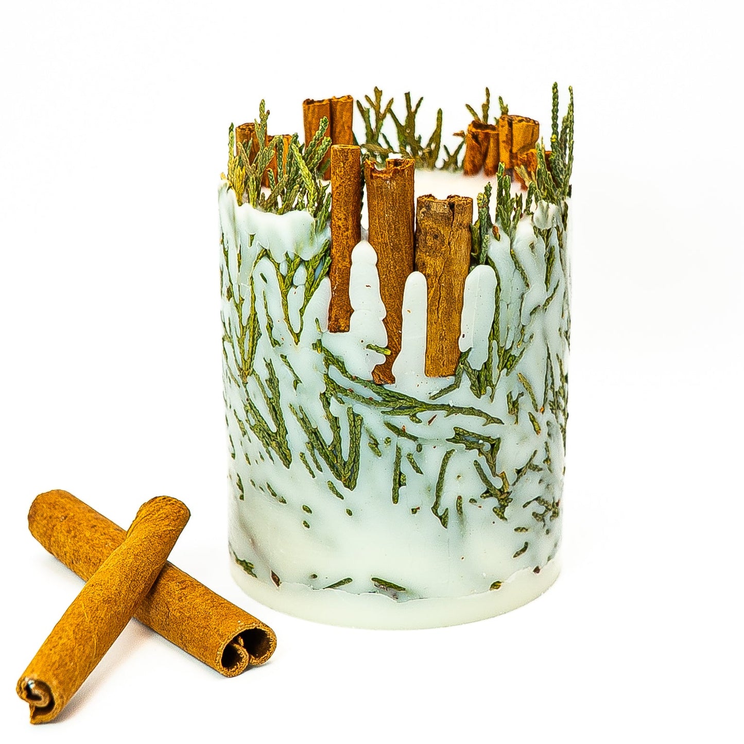 Handmade botanical pillar candle with embedded evergreen leaves and whole cinnamon sticks.