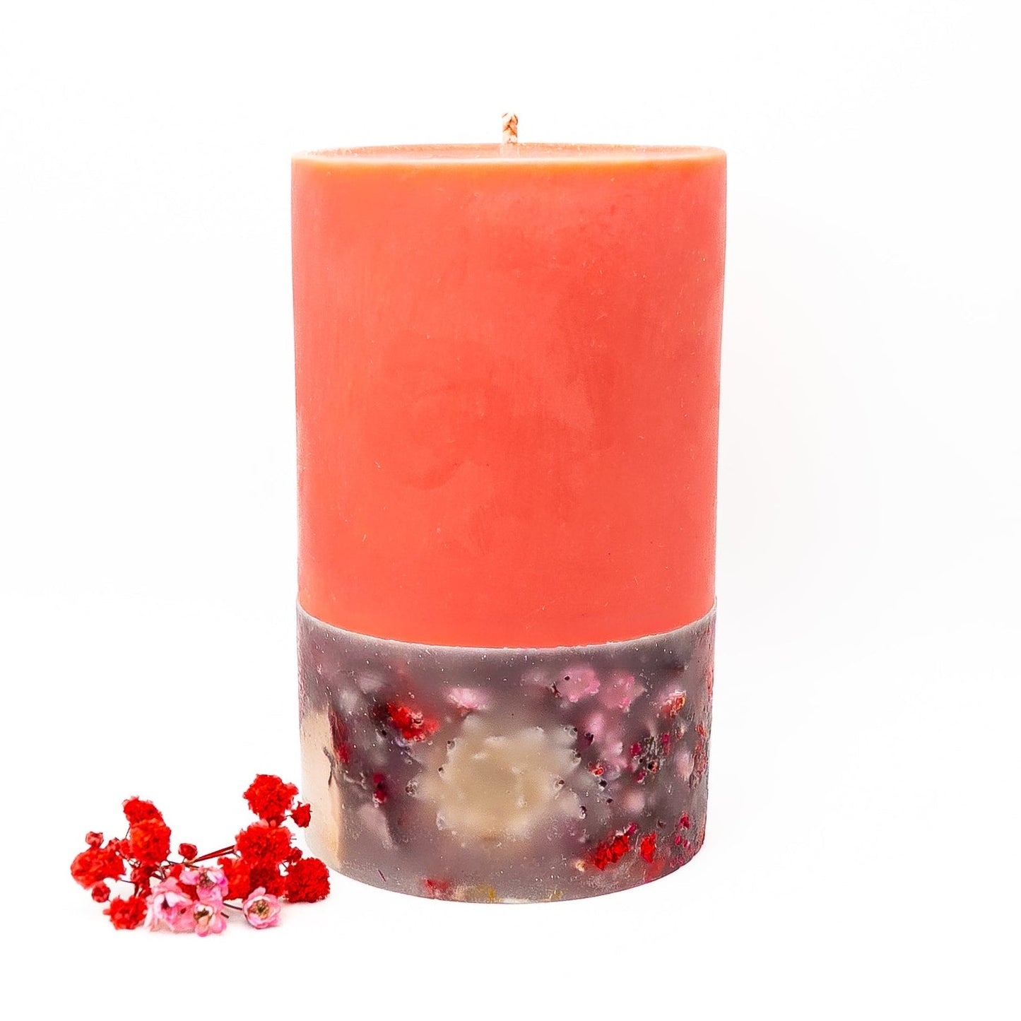 Layered red soy wax pillar candle with decorative botanical base embedded with dried flowers.