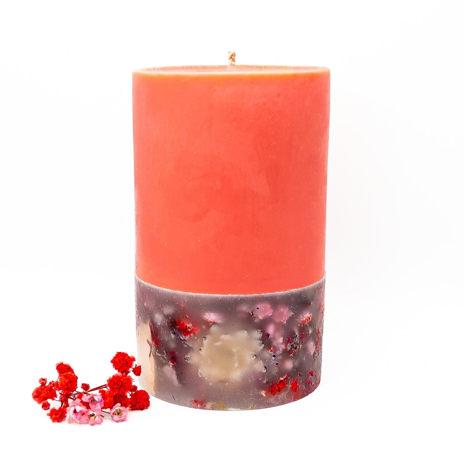 Layered red soy wax pillar candle with decorative botanical base embedded with dried flowers.
