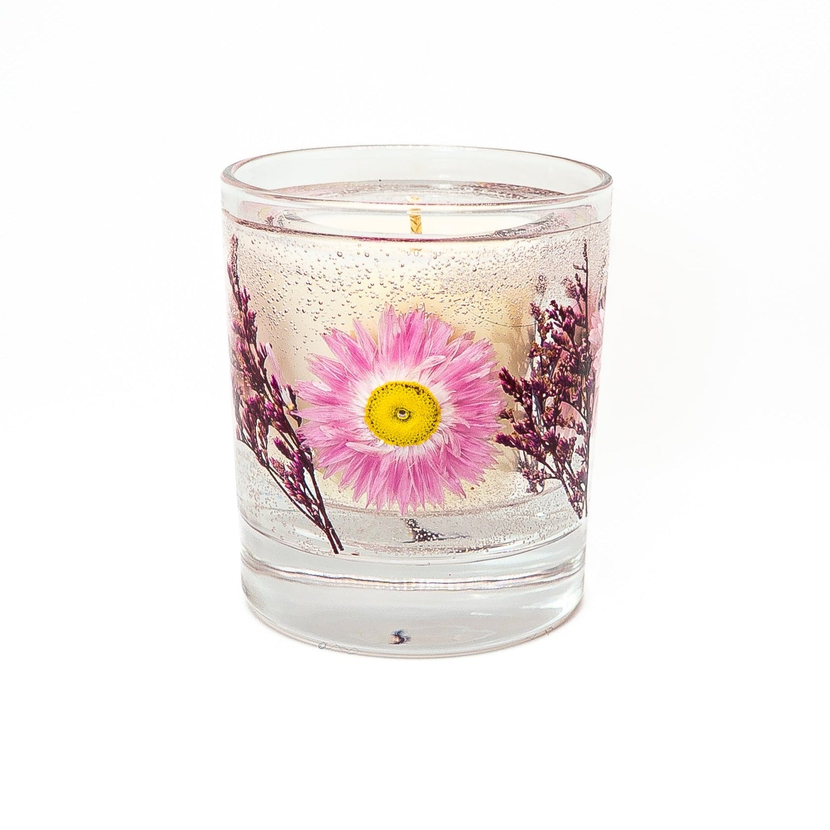 Decorative soy wax candle with transparent gel wax and preserved pink acroclinium flowers in a clear glass container.