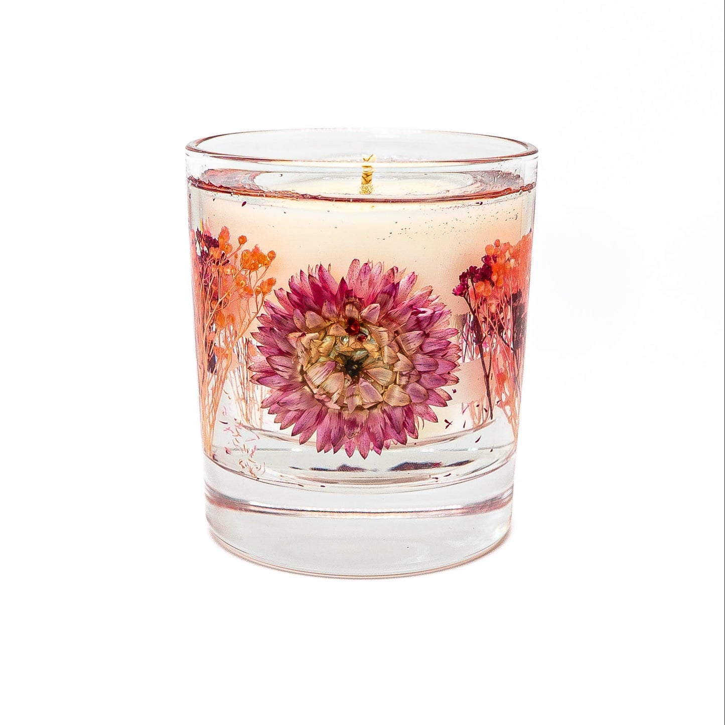 Decorative soy wax candle with transparent gel wax and preserved pink helichrysum flower in a clear glass container.