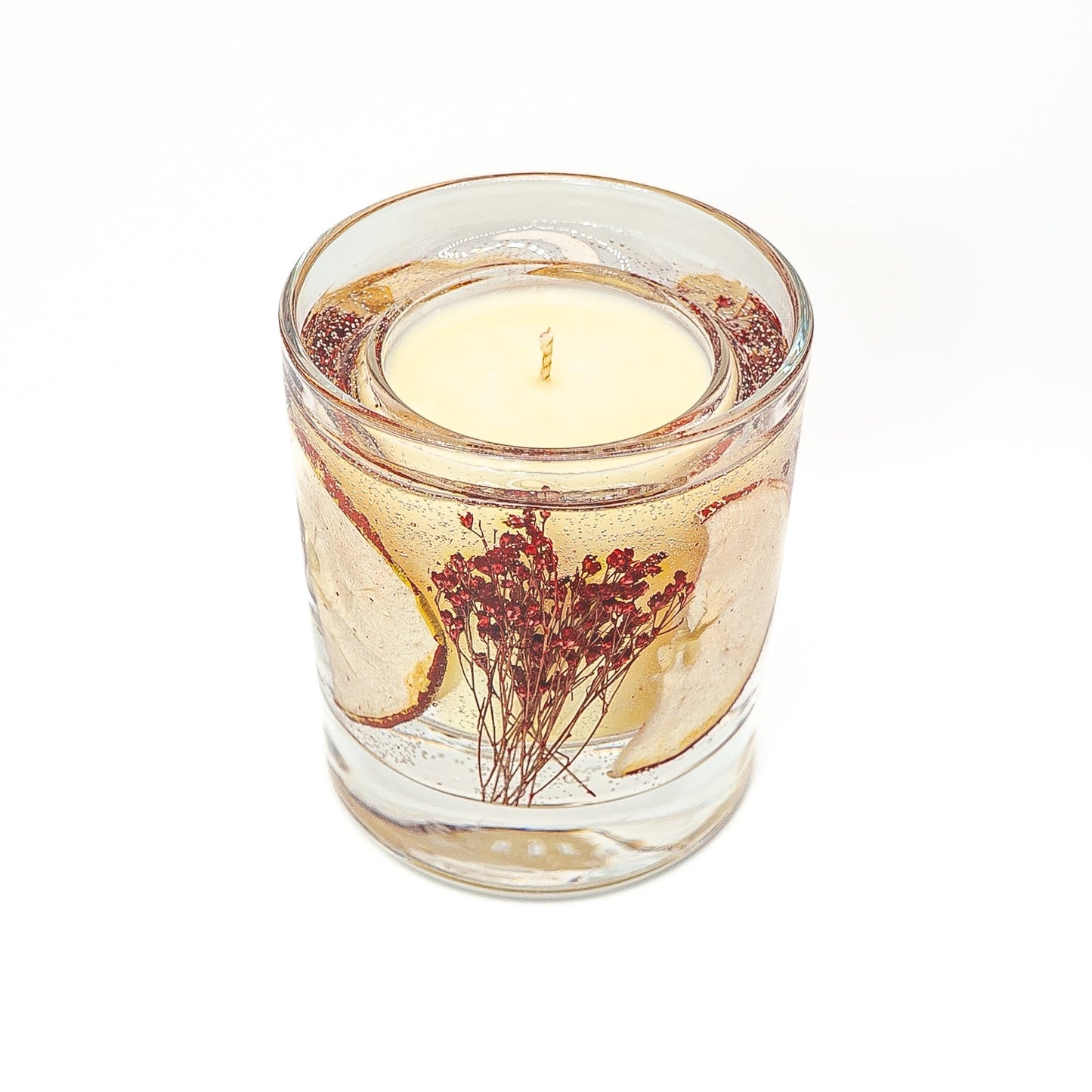 Soy wax candle with gel wax outer layer decorated with dried red apple slice and red botanical stems.