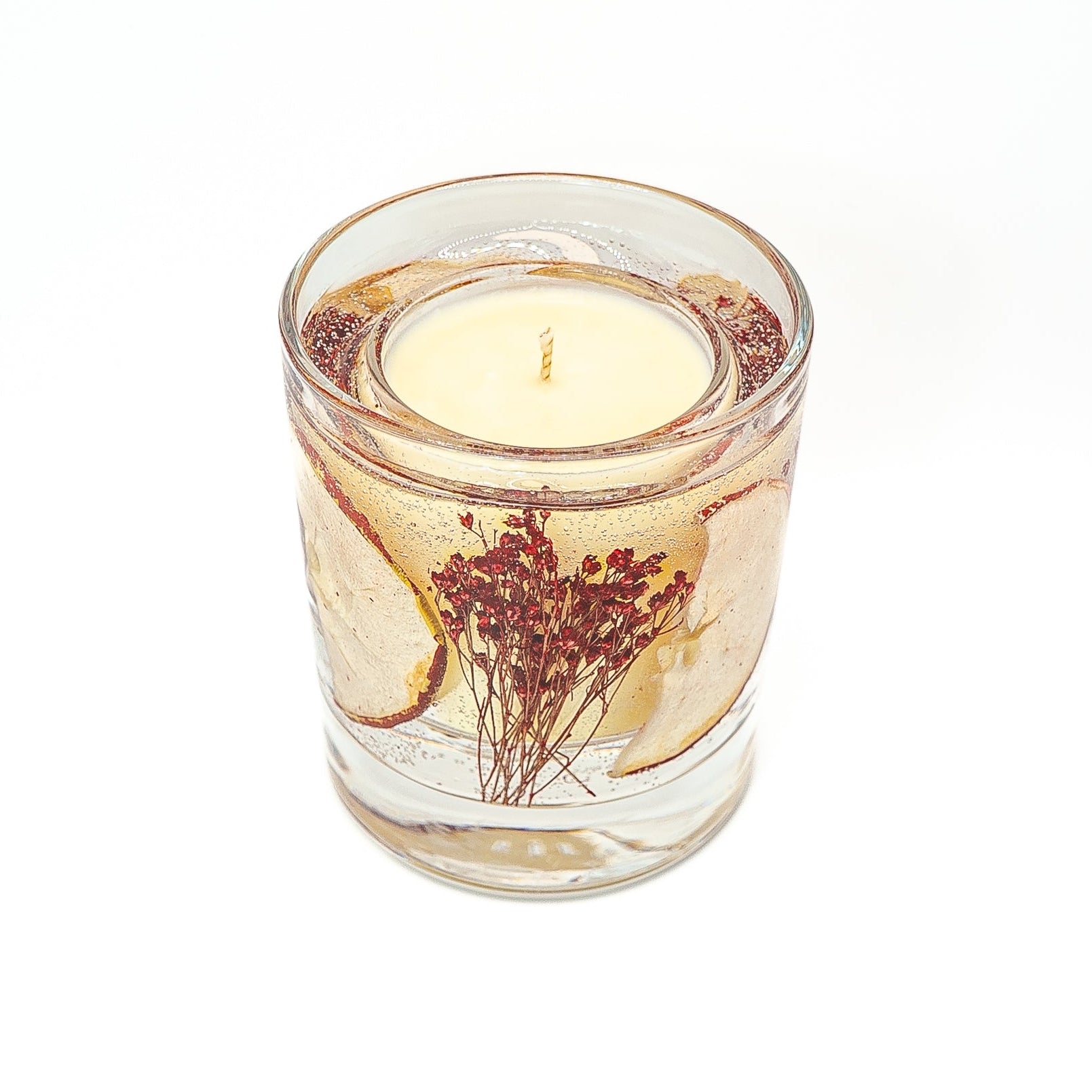Soy wax candle with gel wax outer layer decorated with dried red apple slice and red botanical stems.