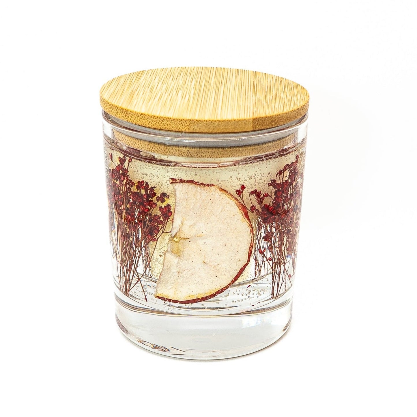 Soy wax candle with clear gel wax layer featuring dried red apple slice and red botanical decorations in a glass jar with bamboo lid.