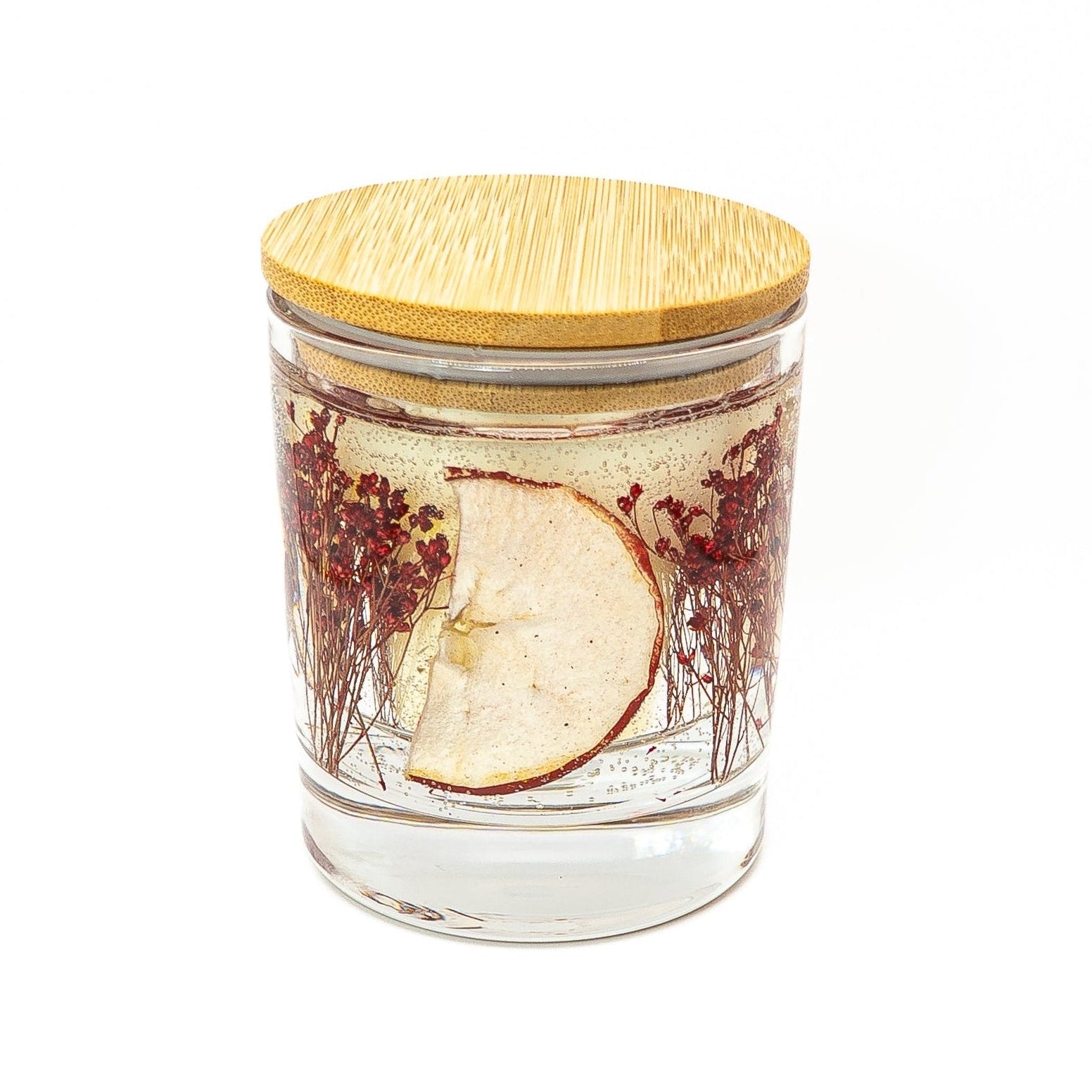 Soy wax candle with clear gel wax layer featuring dried red apple slice and red botanical decorations in a glass jar with bamboo lid.