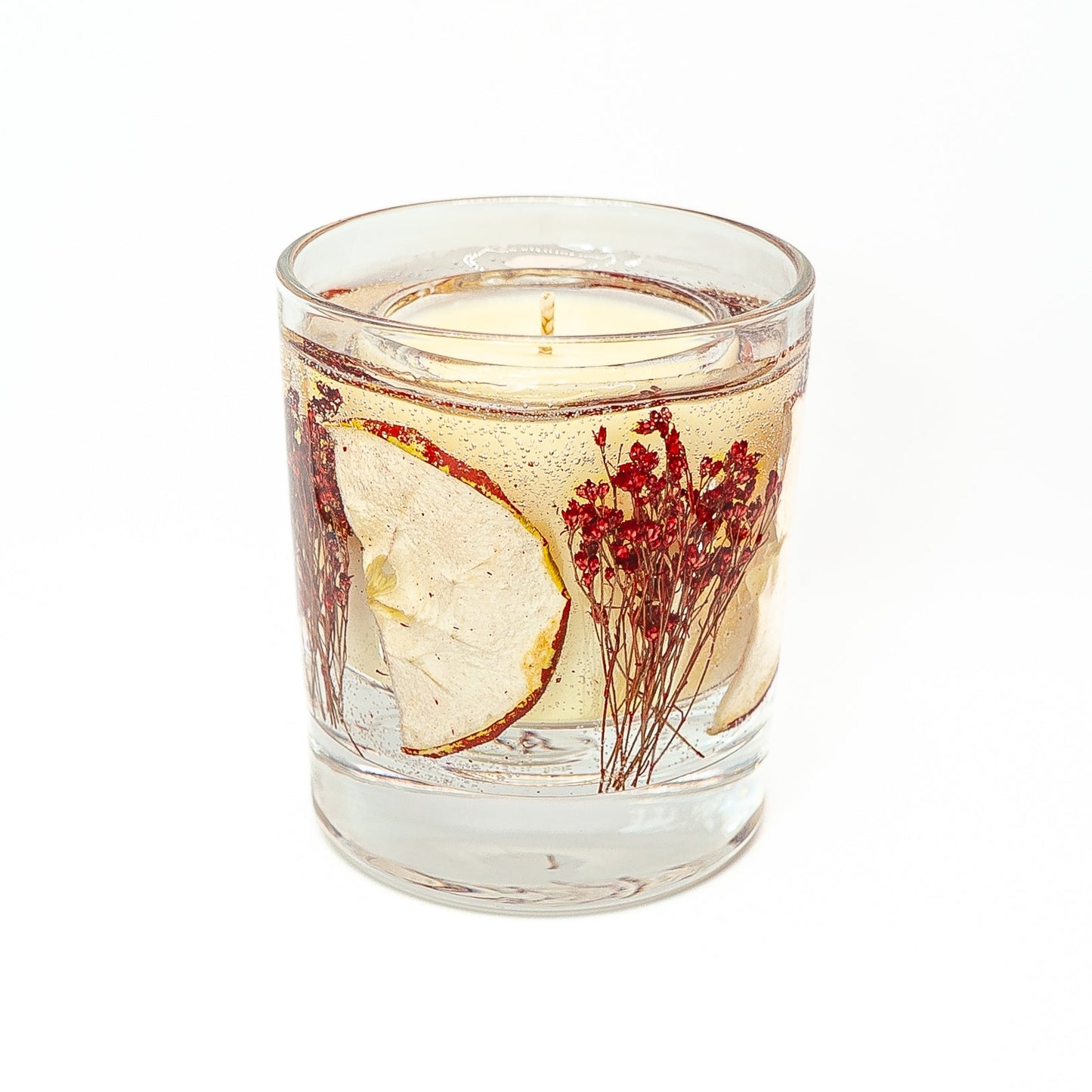 Decorative soy wax candle with clear gel wax featuring dried red apple slice and botanical elements.
