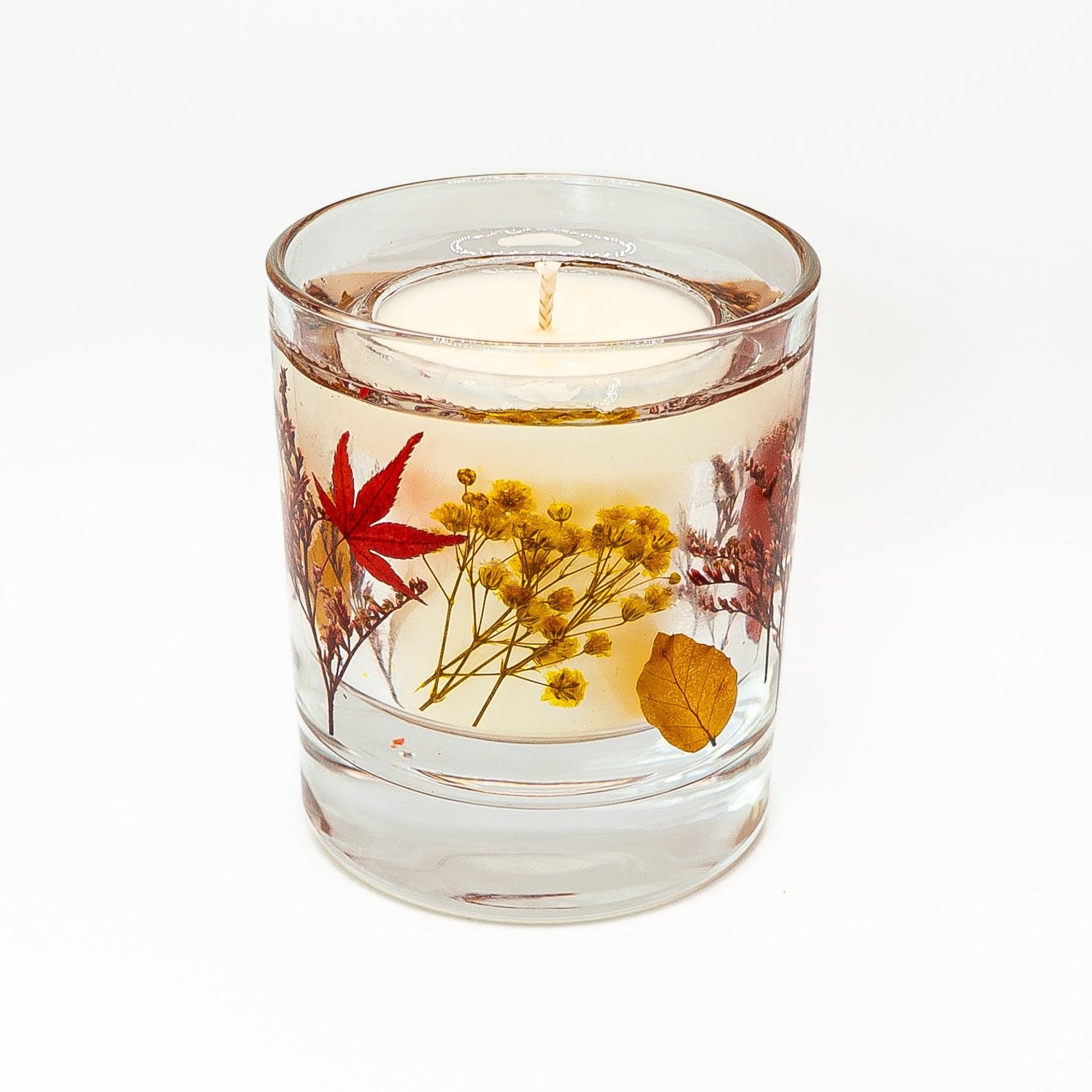 Soy wax candle with clear gel wax outer layer decorated with red leaves and natural dried flowers.