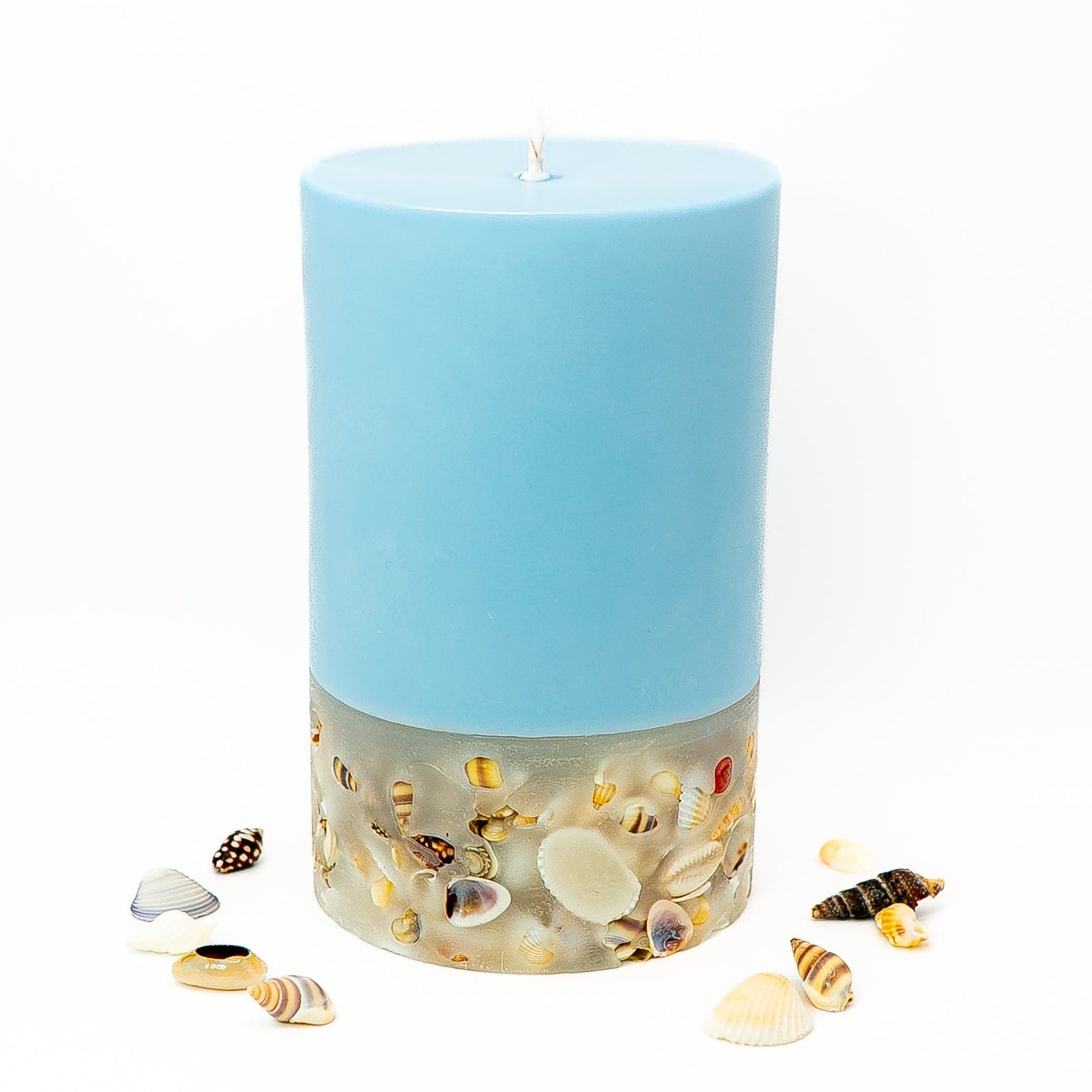 Layered soy wax pillar candle with pastel blue top and seashell-embedded base inspired by coastal décor.