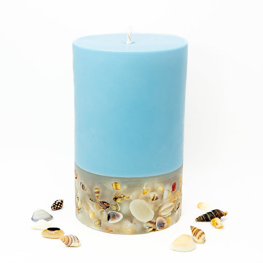 Layered soy wax pillar candle with pastel blue top and seashell-embedded base inspired by coastal décor.