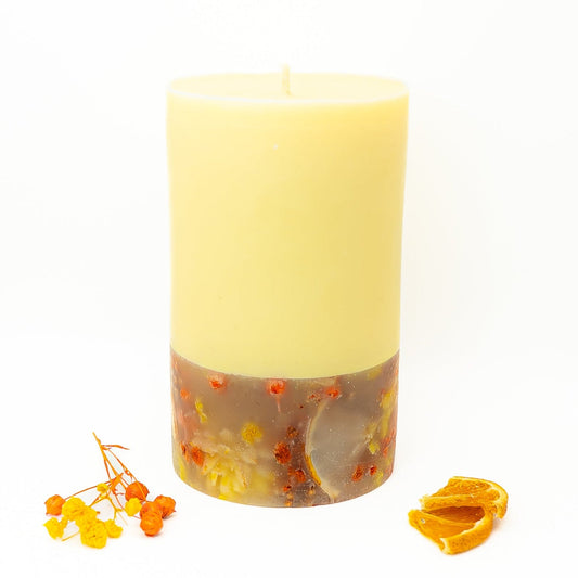 Yellow soy wax pillar candle with dried citrus slices and botanical elements embedded in the base.